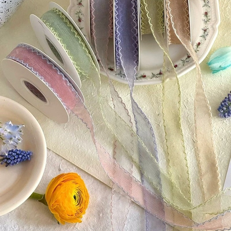 Seven colors of scallop edge sheer ribbon draped across vintage floral plate with rolls in blush sage lavender ivory and dried flowers — Sivonna wedding floral ribbon