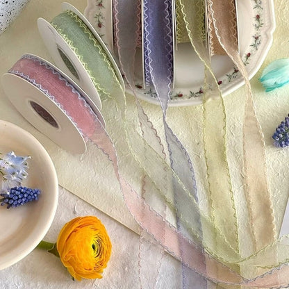 Seven colors of scallop edge sheer ribbon draped across vintage floral plate with rolls in blush sage lavender ivory and dried flowers — Sivonna wedding floral ribbon