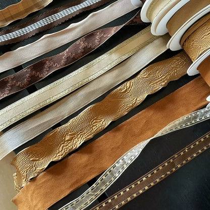 Nine rolls of brown wired edge ribbon on white spools showing full color range from ivory to espresso — Sivonna wired ribbon collection
